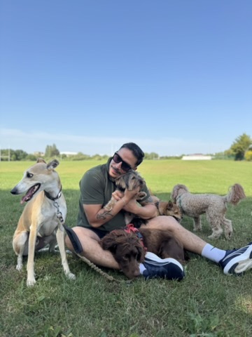 Cristian sitting on the grass surrounded by dogs